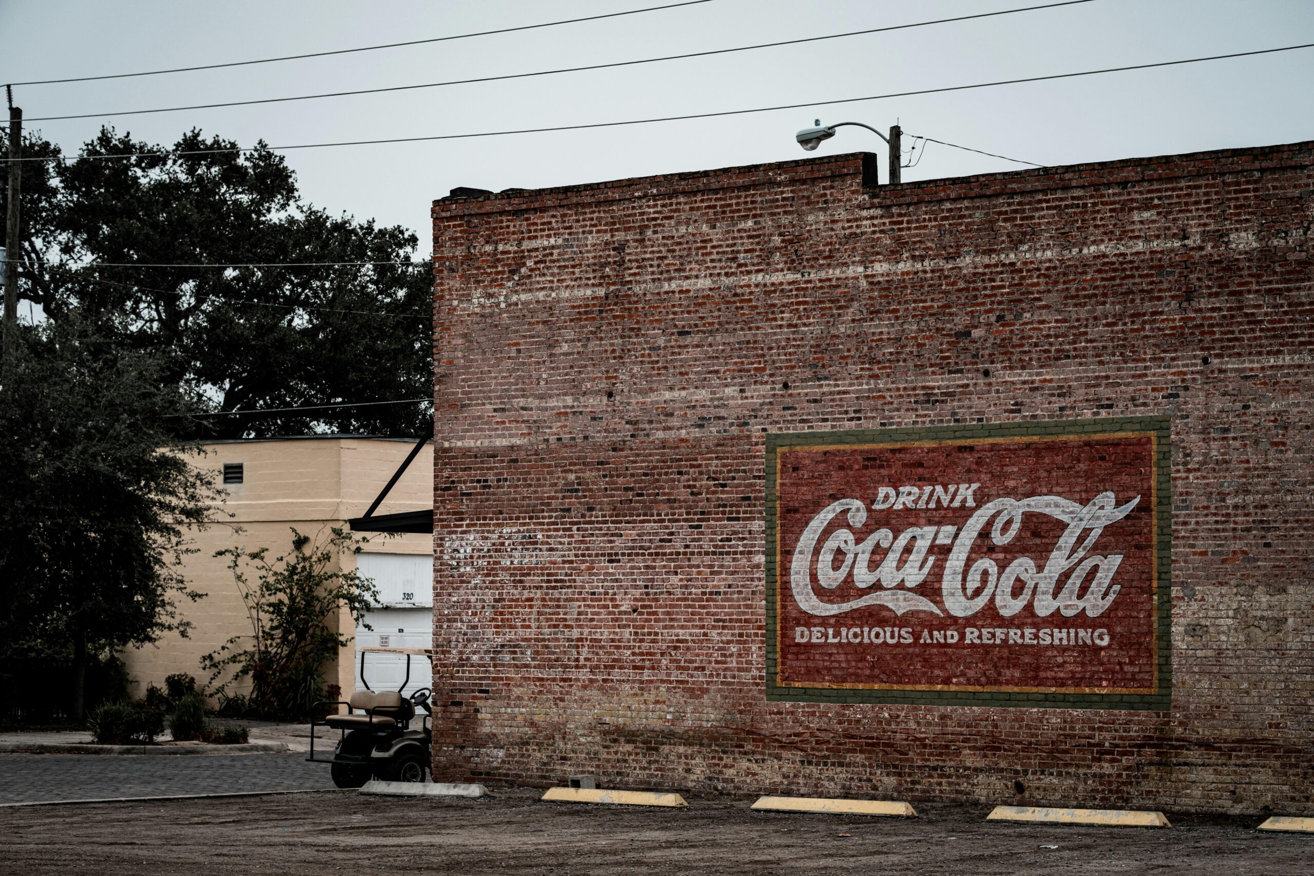 A vintage Coca-Cola mural on a brick wall in an urban parking area.